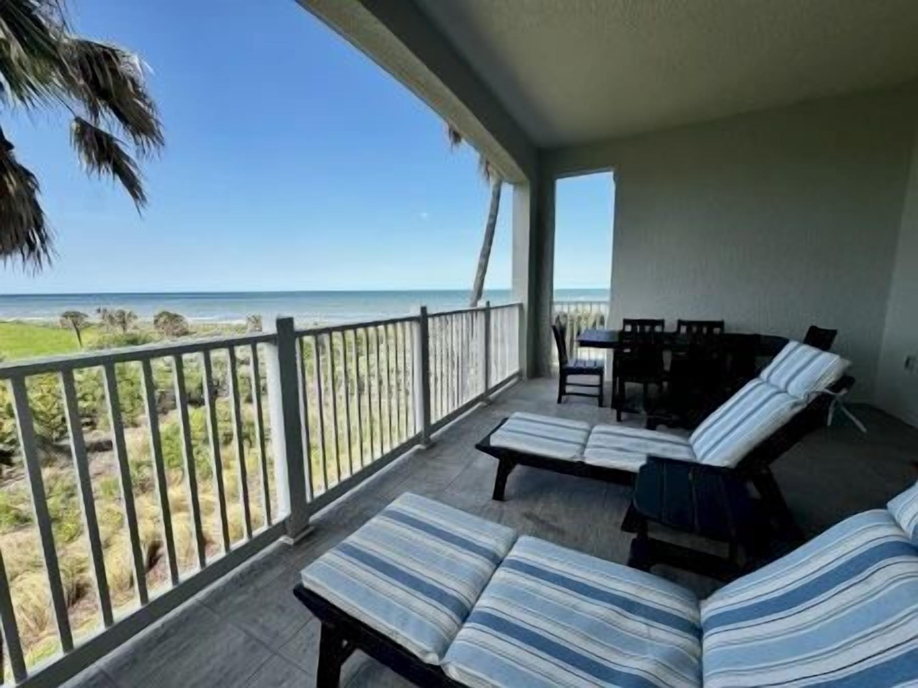 A balcony with a view of the ocean, a seating area with striped cushions, and a table.