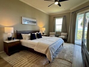 A bedroom with a bed, nightstands, a ceiling fan, and a view of the outdoors. - Ocean View Condo w/ Balcony, Pools & Resort Access (Palm Coast)