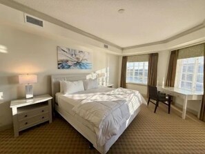 A hotel room with a bed, a desk, a chair, a lamp, and a window. - Waterfront 2BR Condo w/ Pool + Resort Access (Palm Coast)