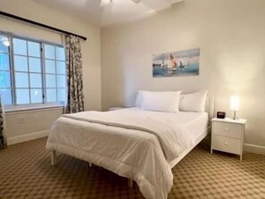 A hotel room with a bed, a nightstand, a window with curtains, and a painting on the wall. - Waterway-View Condo w/ Hammock Beach Resort Access (Palm Coast)