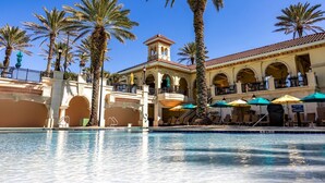 Un hotel amb piscina, palmeres i zones d'estar a l'aire lliure amb ombrelles.