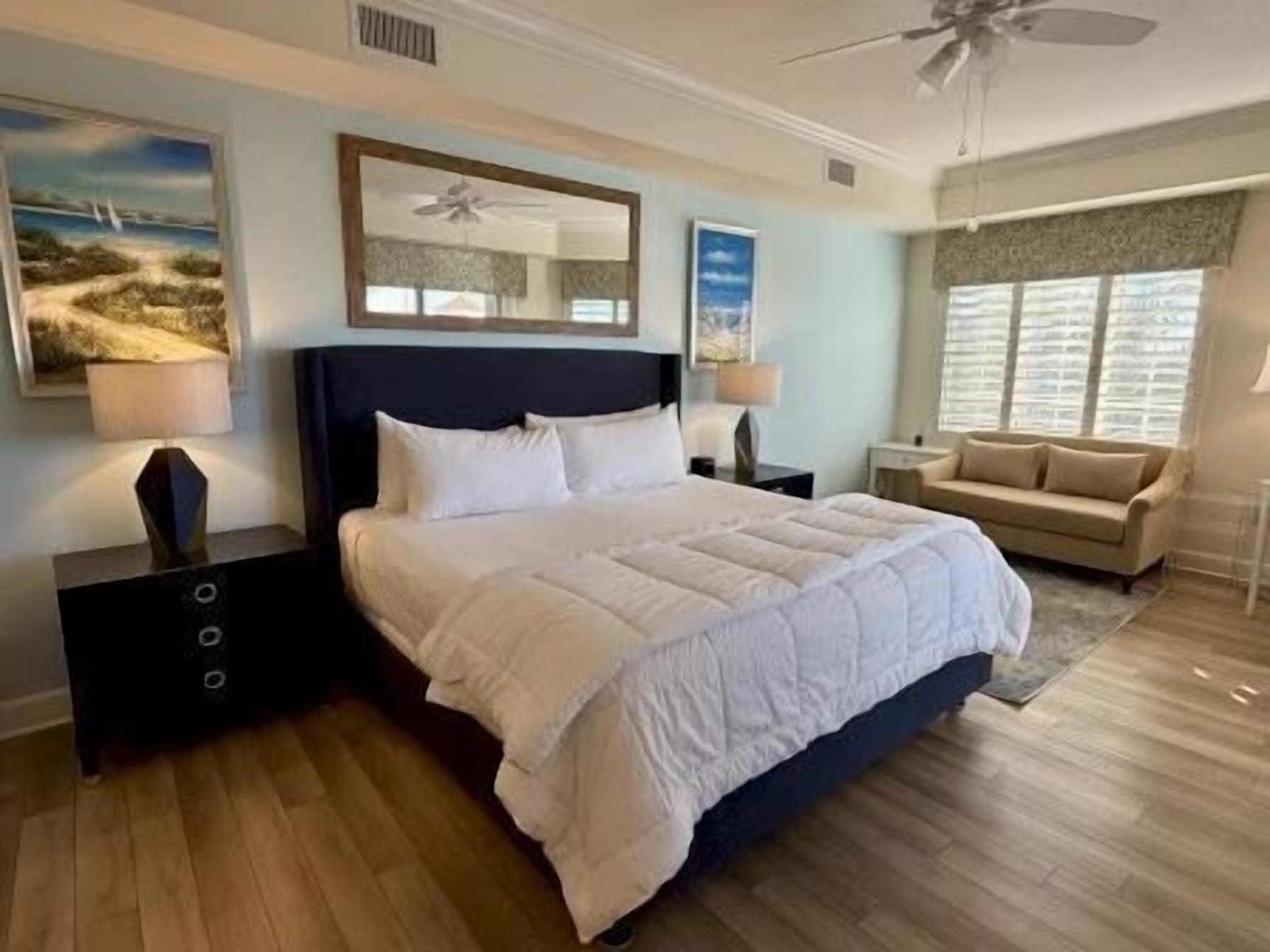 Ein Schlafzimmer mit einem großen Bett, Nachttischen, einem Nachtlicht und einem Deckenventilator, sowie einem Fenster mit Jalousien.