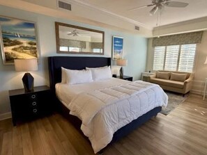 Een slaapkamer met een groot bed, nachtkastjes, een ventilator en een raam met zonwering.