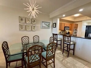 A dining area with a glass table and wooden chairs, a kitchen with wooden cabinets, and a ceiling light fixture. - Waterfront 2BR Condo | Hammock Beach Resort Access (Palm Coast)