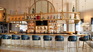 Zona de bar con barra curva, múltiples estantes de botellas y taburetes azules.