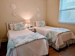 A bedroom with two beds, a nightstand, a lamp, and starfish decorations on the wall. - Shorefront 3BR Condo | Hammock Beach Resort Access (Palm Coast)