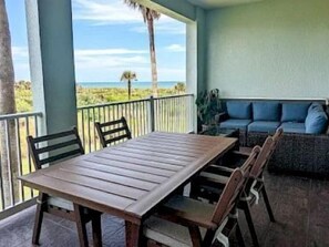A wooden table with chairs on a balcony with a view of the beach. - Shorefront 3BR Condo | Hammock Beach Resort Access (Palm Coast)