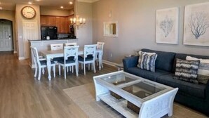 A modern living room with a sofa, coffee table, and dining area with chairs. - Ocean-View 3BR Condo w/ Pools | Resort Access (Palm Coast)