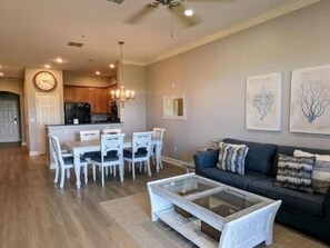 A modern living room with a sofa, coffee table, and dining area with chairs. - Ocean-View 3BR Condo w/ Pools | Resort Access (Palm Coast)