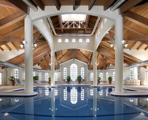 Piscina interna com teto alto, vigas de madeira e grandes janelas.