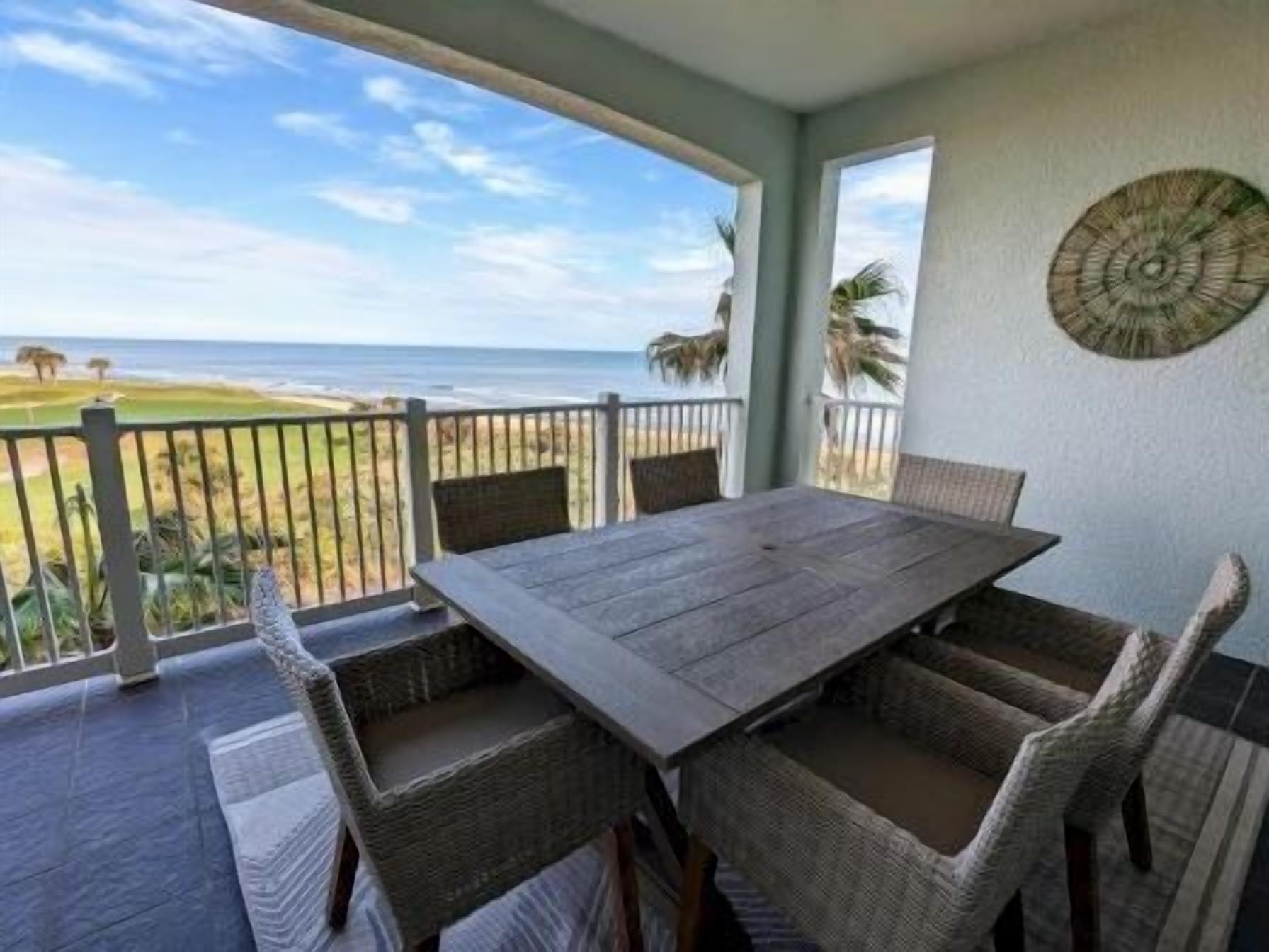 Überdachte Terrasse im Freien mit Tisch und Stühlen, mit Blick auf einen Strand.