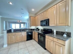 A kitchen with wooden cabinets, a black stove, and granite countertops. - Oceanfront 3BR Condo w/ Game Room + Resort Access (Palm Coast)