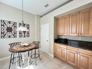 A dining area with a round table and chairs, a pendant light, and wooden cabinets. - Oceanfront 3BR Condo | Hammock Beach Resort Access (Palm Coast)