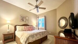 Quarto com cama, mesa de cabeceira, abajur, ventilador de teto, janela e espelho em uma cômoda.