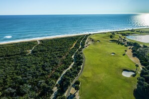 Luftaufnahme eines Küsten-Golfplatzes mit Strand, üppiger Vegetation und freiem Blick auf den Ozean.