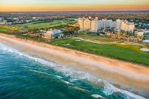 Ein Luftbild eines Küstenhotels mit mehreren Gebäuden, einem Golfplatz und direktem Zugang zum Strand.