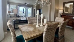 Uma área de refeições com mesa de madeira, cadeiras de vime e um lustre.