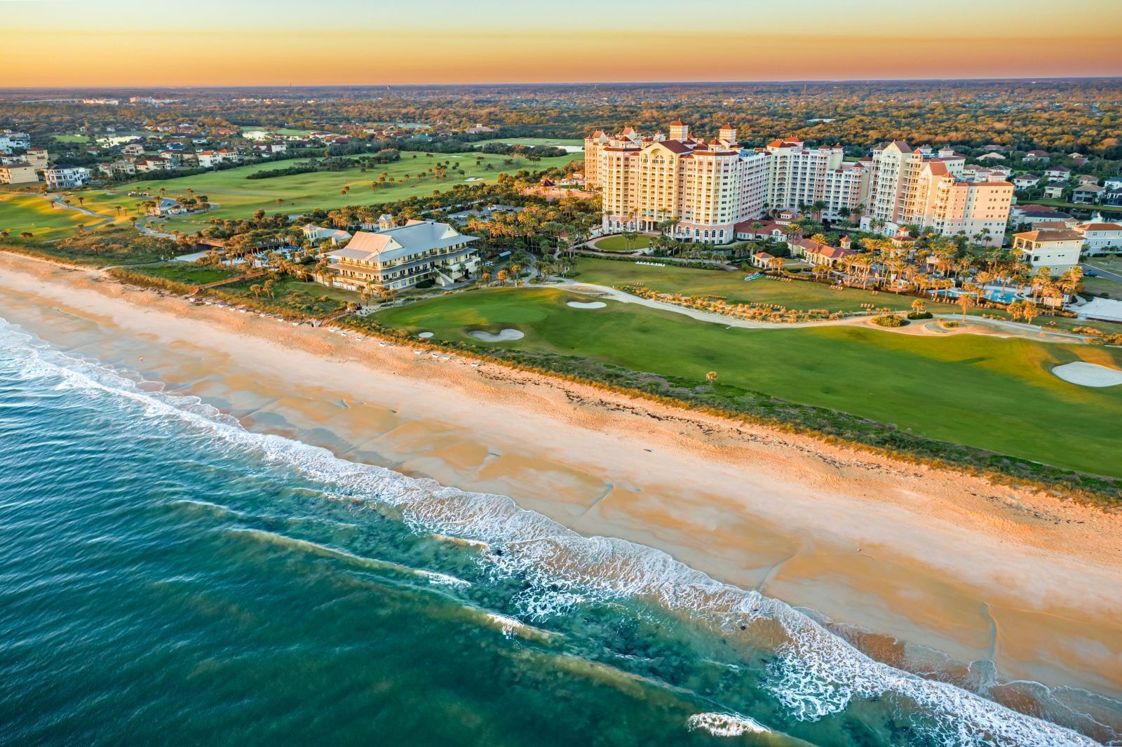 Luchtbeeld van een kusthotel met meerdere gebouwen, een golfbaan en een strand.