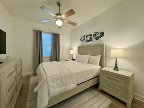 A bedroom with a bed, nightstands, a dresser, a ceiling fan, and a window with curtains. - Lakeside 3BR Condo | Balcony, Pool + Resort Access (Palm Coast)