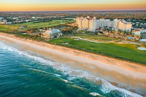 Ein Luftbild eines Küstenhotels mit mehreren Gebäuden, einem Golfplatz und direktem Zugang zum Strand.