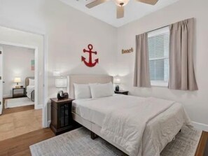 Ein Schlafzimmer mit einem Bett, Nachttischen, einem Deckenventilator und einem Fenster mit Vorhängen.