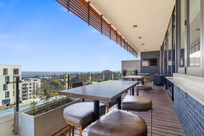 Eine moderne Terrassengrundstück mit einem langen Tisch und Sitzgelegenheiten, mit Blick auf eine Stadtlandschaft.