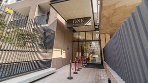 Moderni hotellin sisäänkäynti, jossa on lasiovi, kyltti, jossa lukee ”ONE ROSEBANK”, ja punainen matto, joka johtaa sisäänkäynnille.