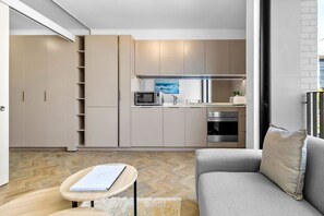 A modern kitchen with built-in appliances, a dining area with a grey sofa, and a wooden herringbone floor. - One Rosebank 151 - One Bedroom Apartment, Sleeps 2 (Johannesburg)