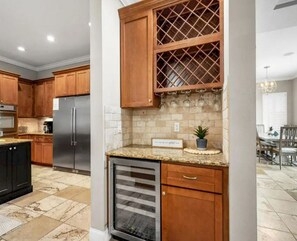 A kitchen with wooden cabinets, a stainless steel refrigerator, a wine rack, and a built-in oven. - Lake-View 11BR House | Heated Pool & Resort Access (Palm Coast)