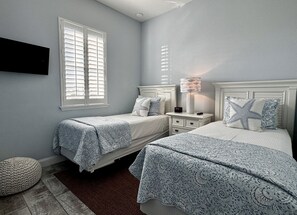 A bedroom with two beds, a nightstand, a lamp, and a wall-mounted TV. - Lake-View 5BR Home w/ Hammock Beach Resort Access (Palm Coast)