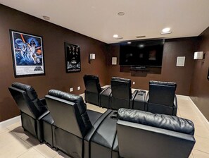 Ein Heimkino mit schwarzen Ledersesseln, einem großen Flachbildfernseher und Filmplakaten an der Wand.