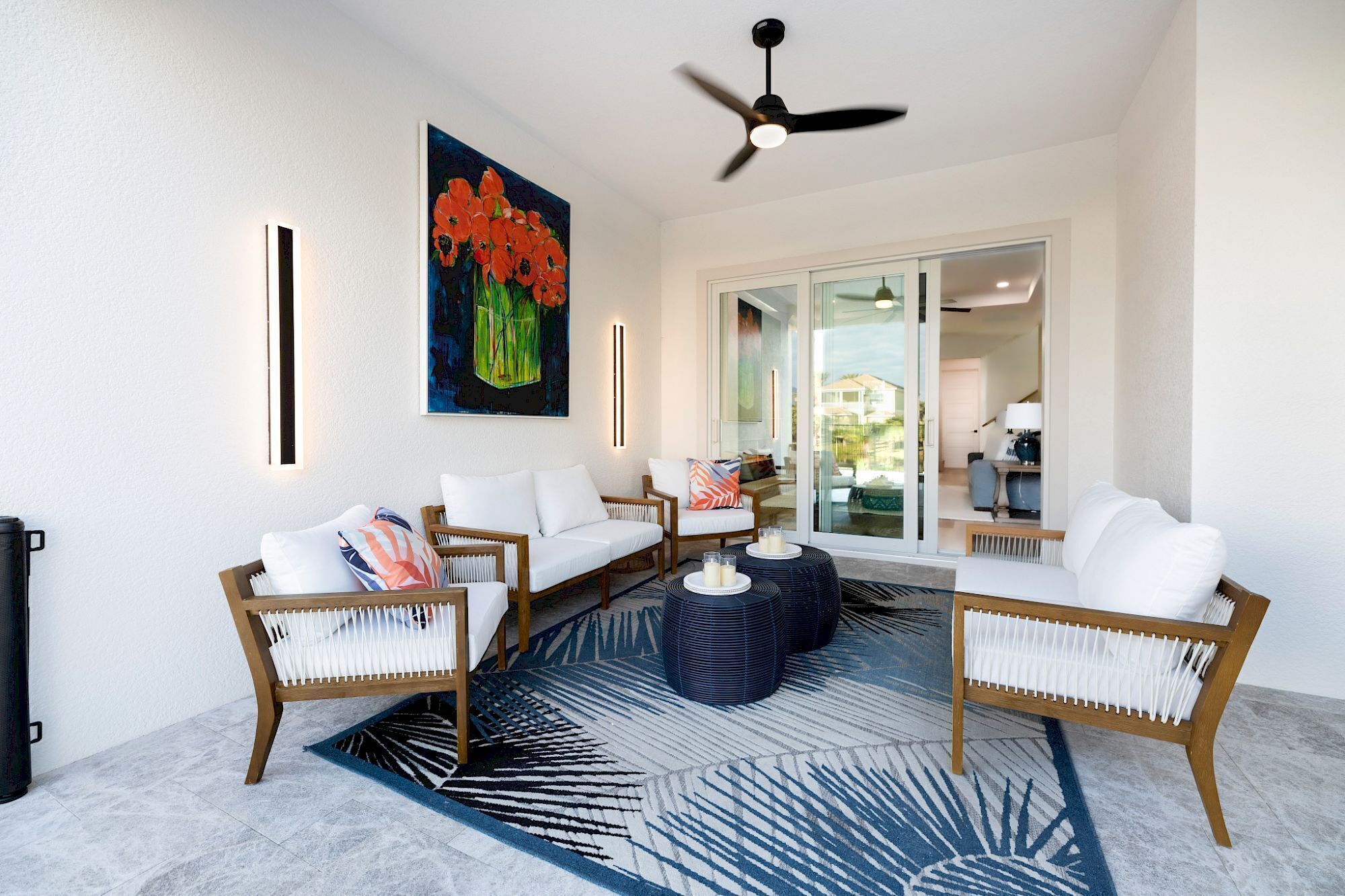 A modern living room with a ceiling fan, a large painting, and a view through glass doors.