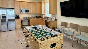 Een moderne keuken met een tafelvoetbalspel, een grote televisie en houten kasten.