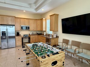 A modern kitchen with a foosball table, a large TV, and wooden cabinets. - Spacious 3BR Home w/ Rooftop Deck + Resort Access (Palm Coast)
