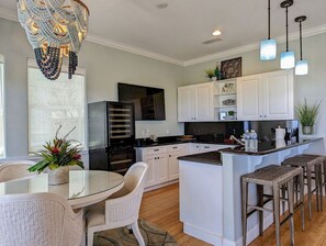 A modern kitchen with white cabinetry, a central island, bar stools, and pendant lighting. - Oceanview 5BR Home w/ Pool, Beach & Resort Access (Palm Coast)