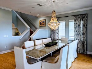 Uma sala de jantar moderna com mesa de vidro, cadeiras estofadas brancas, um candelabro e uma escada.