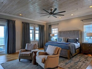 Quarto com cama grande, duas poltronas, ventilador de teto e vista para o exterior.
