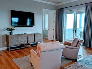 A living room with a flat-screen TV, a patterned cabinet, two armchairs, a rug, and a view of the outdoors through a sliding glass door. - Oceanview 5BR Home w/ Hammock Beach Resort Access (Palm Coast)