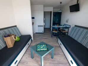 A compact living space with a sofa, a small table, and a dining area. - T2 face au Lac | À 100 m de la plage | Piscine (Vieux-Boucau-les-Bains)