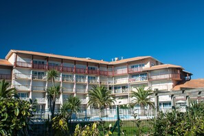 A multi-story hotel with balconies, a swimming pool, and palm trees. - T2 face au Lac | À 100 m de la plage | Piscine (Vieux-Boucau-les-Bains)