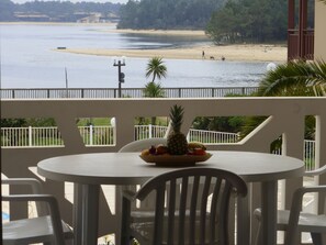 A balcony with a table and chairs, overlooking a beach and water. - En bord du lac | À 300 m de la mer | Accès piscine (Vieux-Boucau-les-Bains)