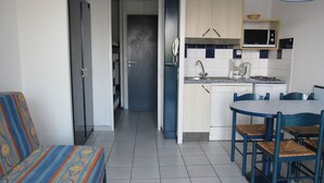 Una cocina compacta con microondas, pileta y pequeño refrigerador. Hay una mesa de comedor con sillas y un sofá en el área de estar contigua.