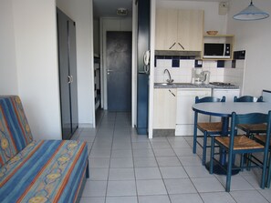 A compact kitchen with a microwave, sink, and a small refrigerator. There is a dining table with chairs and a sofa in the adjacent living area. - En bord du lac | À 300 m de la mer | Accès piscine (Vieux-Boucau-les-Bains)