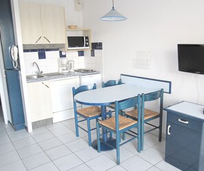 A compact kitchen with a microwave, sink, and a dining area with chairs and a table. - En bord du lac | À 300 m de la mer | Accès piscine (Vieux-Boucau-les-Bains)