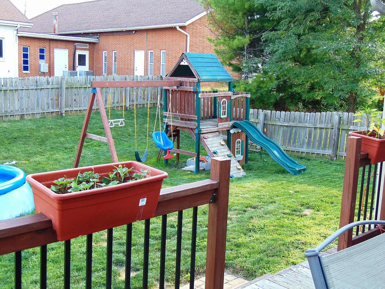 A backyard with a wooden play structure, including a slide and swings, and a small garden bed with plants.