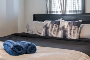 A neatly made bed with a dark headboard, two pillows with a plaid pattern, and a pair of rolled blue towels. - Fire Table Deck · 9 Min to Easton · Sleeps 8 (Columbus)