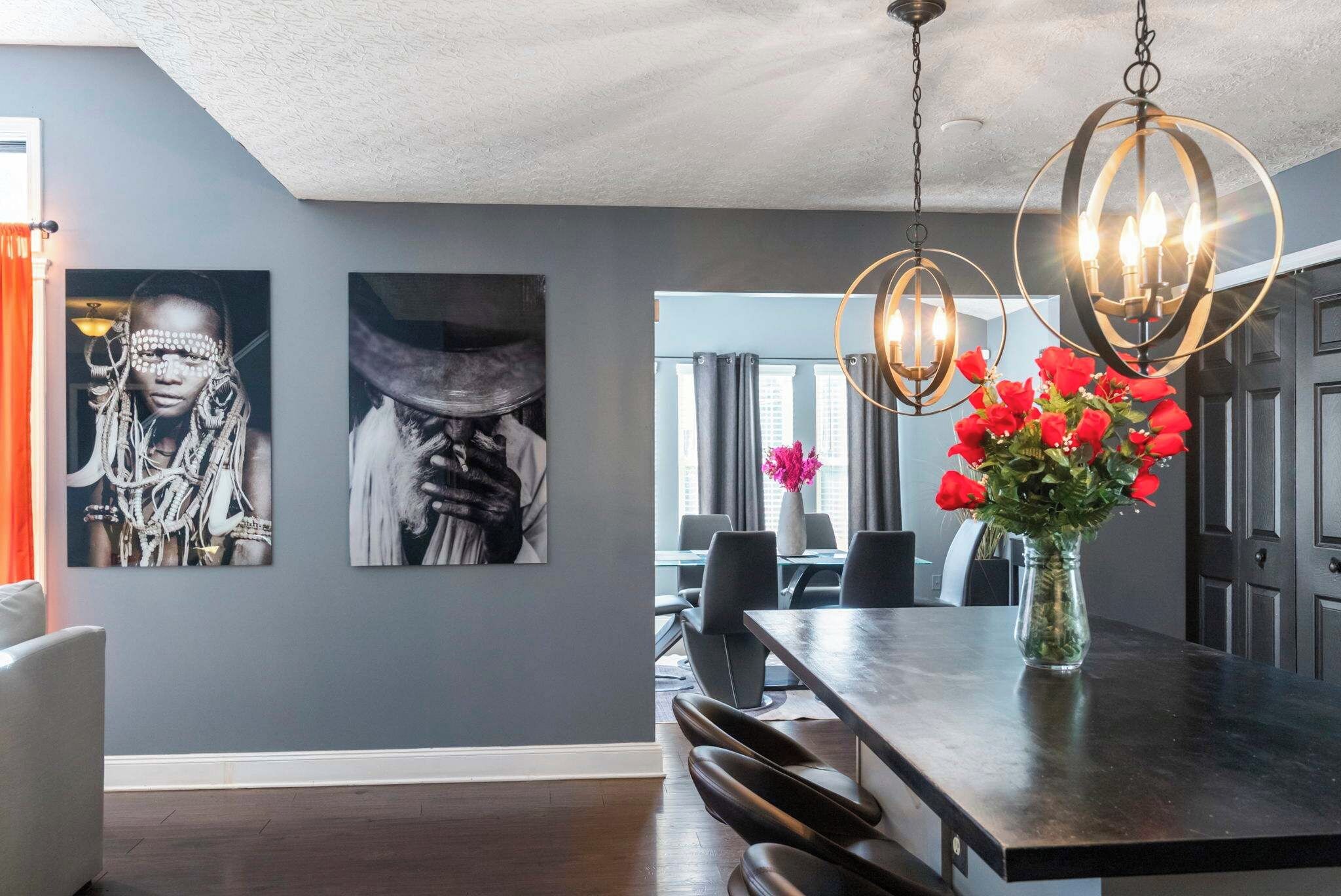 A dining area with a dark wood table, two chairs, a vase with red flowers, and a chandelier.