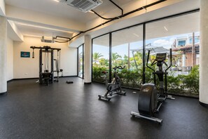 A gym with exercise equipment and large windows overlooking a landscaped area. - Vista Cana | 1 Bedroom with Coworking and Pool (Bavaro)