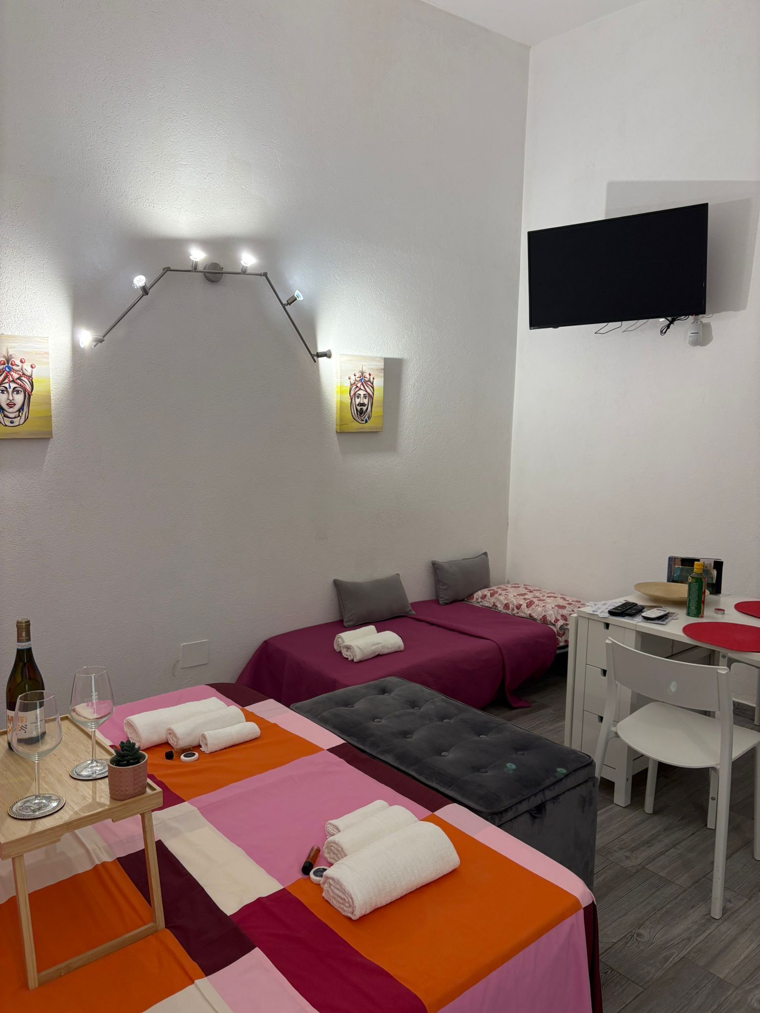 A hotel room with two beds, a desk, a TV, and a wall-mounted light fixture.