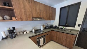 Una cuina moderna amb armaris de fusta, forn de mur, rentamillera i cafetera.